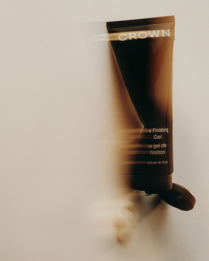 Crown The Finishing Gel product shot. Brown and black tube with brand name and product info on light beige background with motion blur.