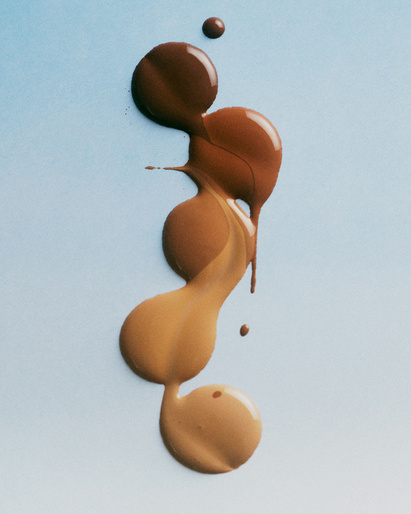 Several shades of foundation makeup in a vertical gradient from dark to light on a soft blue background. Beauty and cosmetic product.