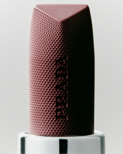 Close-up of a Prada lipstick tube in a mauve color with a textured surface against a light background in a studio setting.
