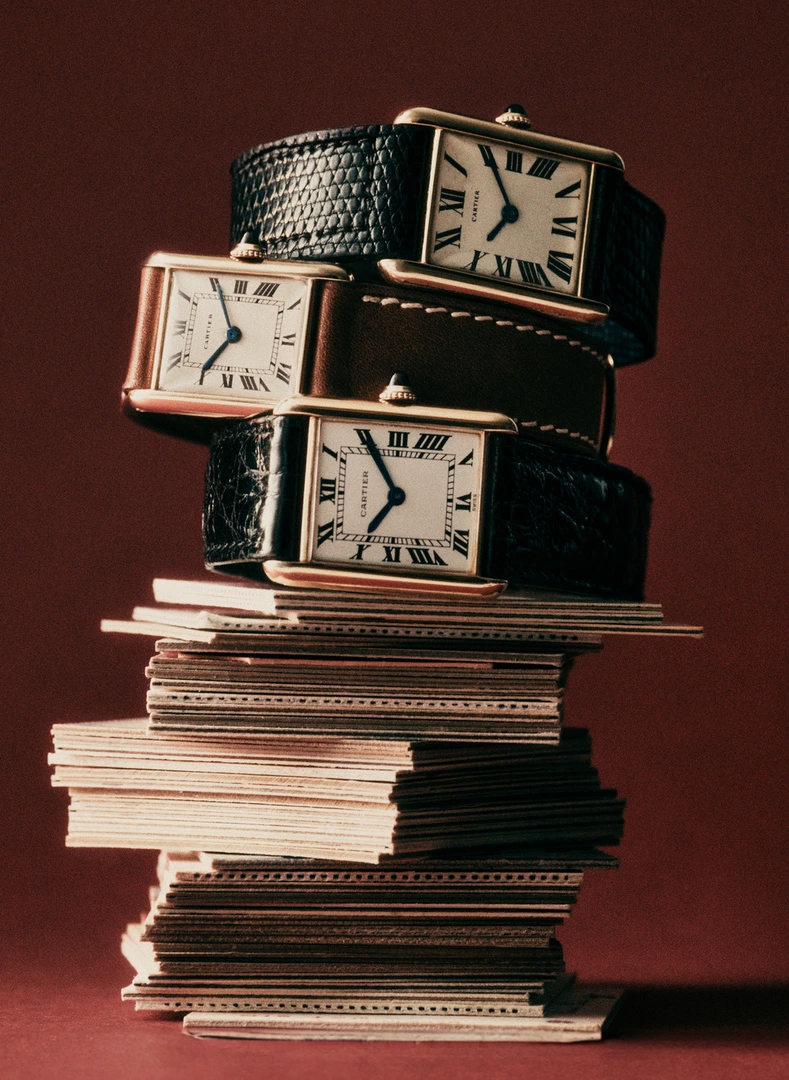 Three luxury wristwatches with leather straps stacked on top of a tall pile of cards against a solid dark red background