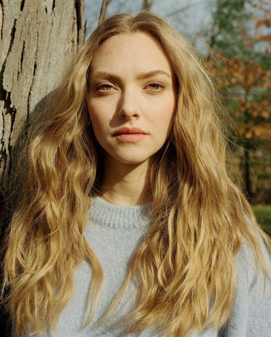 Portrait of a fair-skinned blonde woman in front of a tree, wearing a pale blue sweater, captured in a natural outdoor setting.