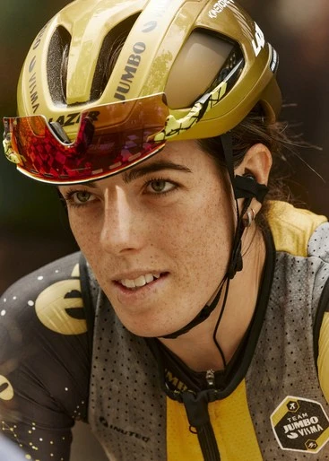 Close-up of a female cyclist wearing a gold helmet and visor, focused on the race ahead, showcasing determination and athletic gear.