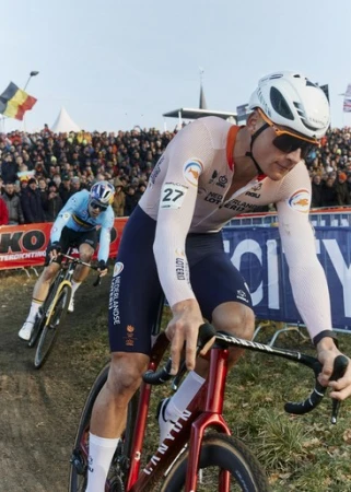 Cyclist in action during a race, wearing a helmet and team gear, with a crowd in the background and racing bike in focus.