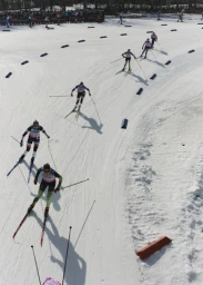 High-angle view of multiple cross-country skiers racing down a snow-covered track lined with blue markers.