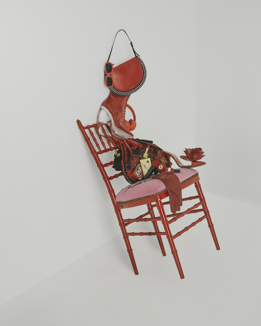 Red chair with purse, sunglasses, headphones, lipstick, and shoes, all in red tones, against a clean white background.