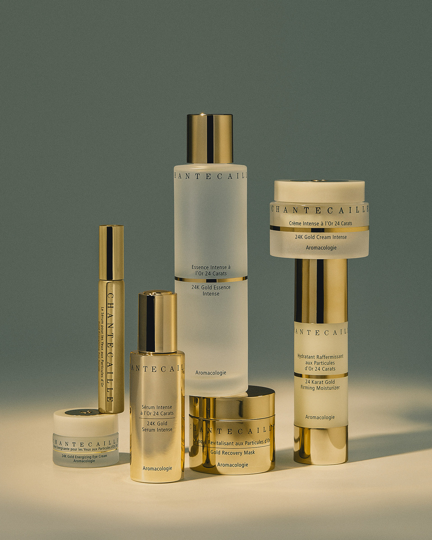 Chantecaille skincare product line featuring gold-tone packaging on a soft teal background in a studio setting, highlighting luxury and beauty.