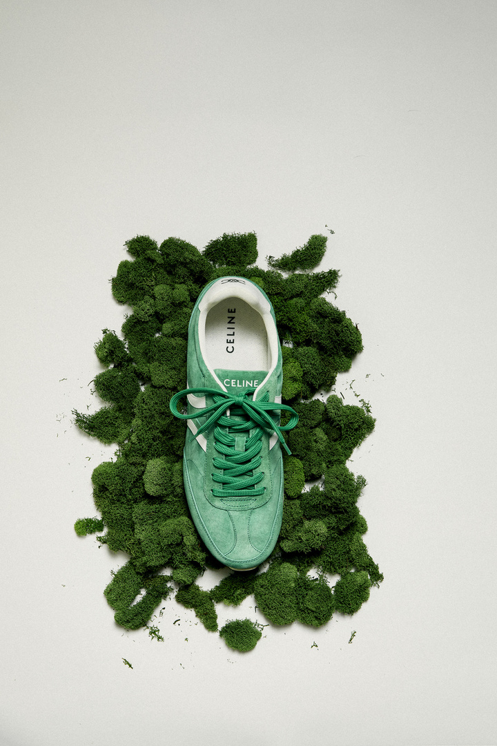 Green Celine sneaker displayed on bed of moss. Overhead shot for product presentation. White background providing contrast and emphasis. 