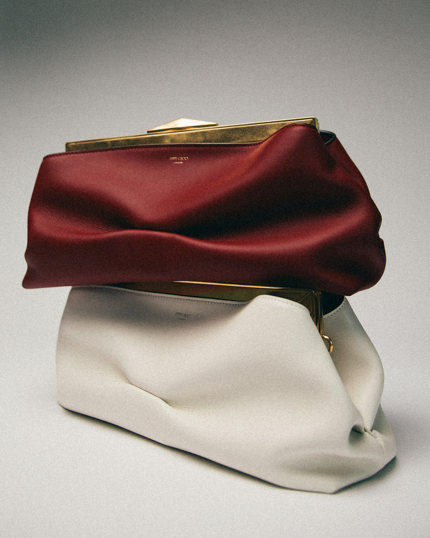 Two leather clutches, one off-white and one burgundy, are stacked on a white surface, against a light grey background in a studio setting.