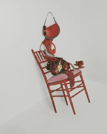 Red chair piled with stacked fashion accessories including handbags boots and sunglasses