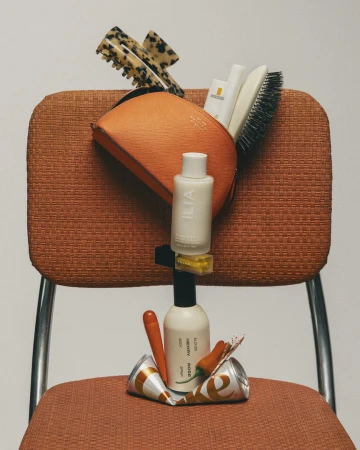 Still life arrangement of beauty products hairbrush and accessories stacked precariously on an orange textured chair