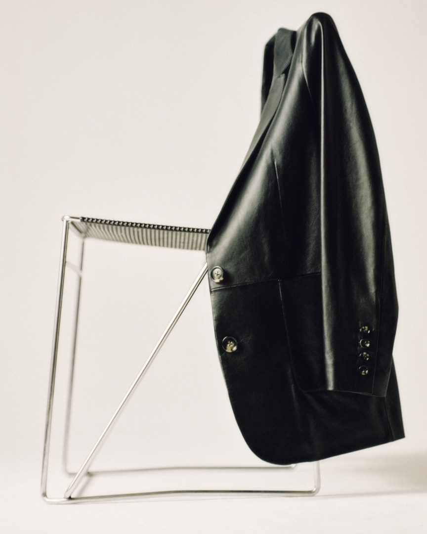 Black leather jacket draped over a modern metal chair against a white backdrop. Clothing item, studio shot, design element.