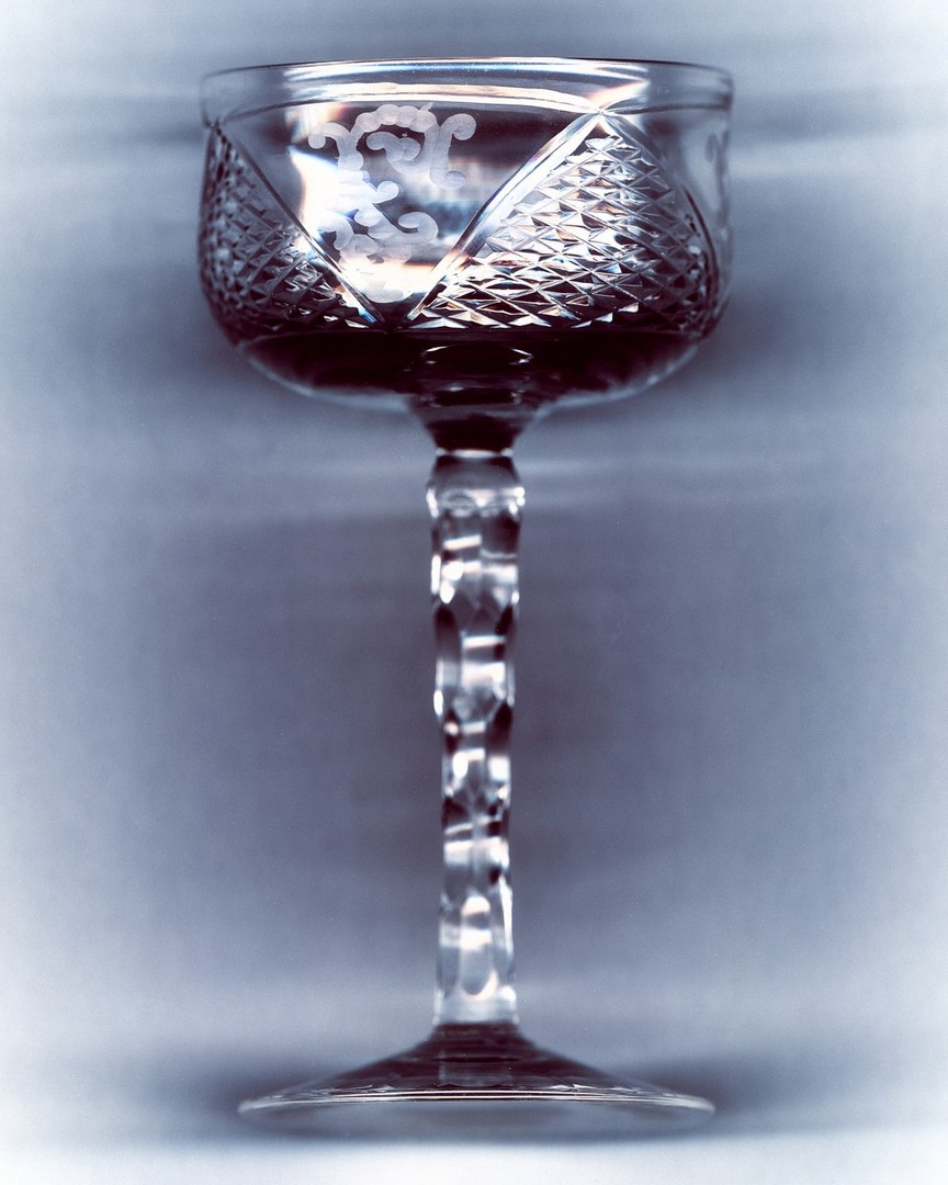 Crystal glass filled with a dark liquid, featuring a tall stem, detailed etching on the glass and a neutral, blurred background.