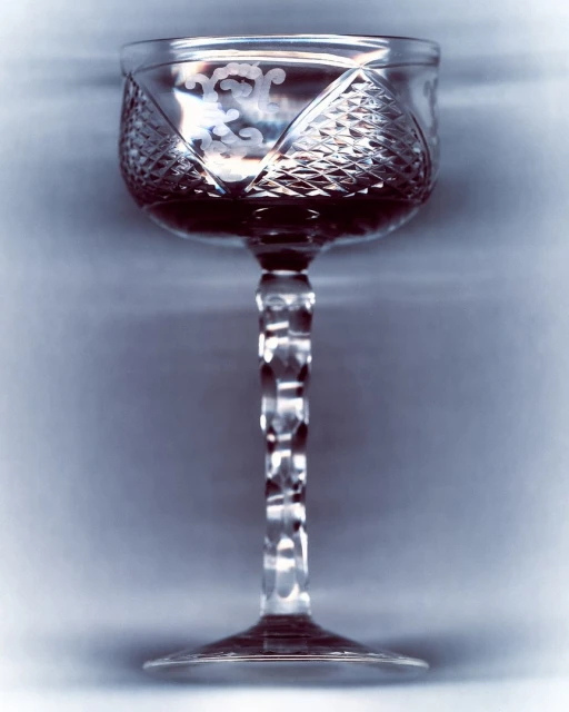 Crystal glass filled with a dark liquid, featuring a tall stem, detailed etching on the glass and a neutral, blurred background.