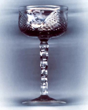 Crystal glass filled with a dark liquid, featuring a tall stem, detailed etching on the glass and a neutral, blurred background.