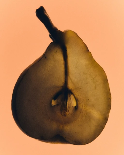 Close-up studio shot of a halved pear with visible seeds, showcasing its translucent texture against a soft orange background.