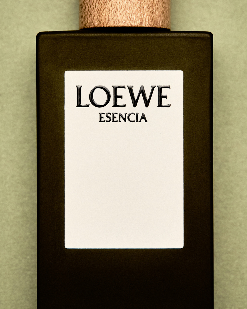 Loewe Esencia perfume bottle on a light green background. Close-up product shot featuring a rectangular bottle with a wooden cap and minimalist label.