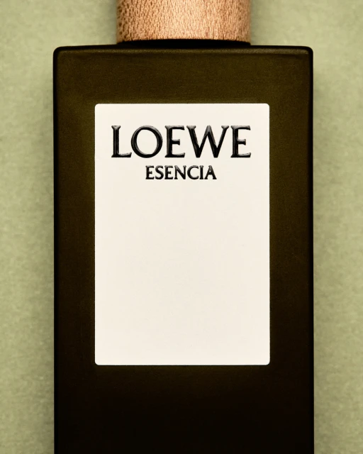 Loewe Esencia perfume bottle on a light green background. Close-up product shot featuring a rectangular bottle with a wooden cap and minimalist label.