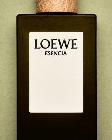 Loewe Esencia perfume bottle on a light green background. Close-up product shot featuring a rectangular bottle with a wooden cap and minimalist label.