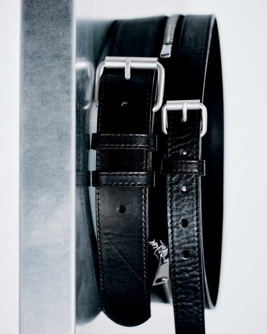 Close-up of a black leather bag with silver zippers and buckle straps against a white backdrop.