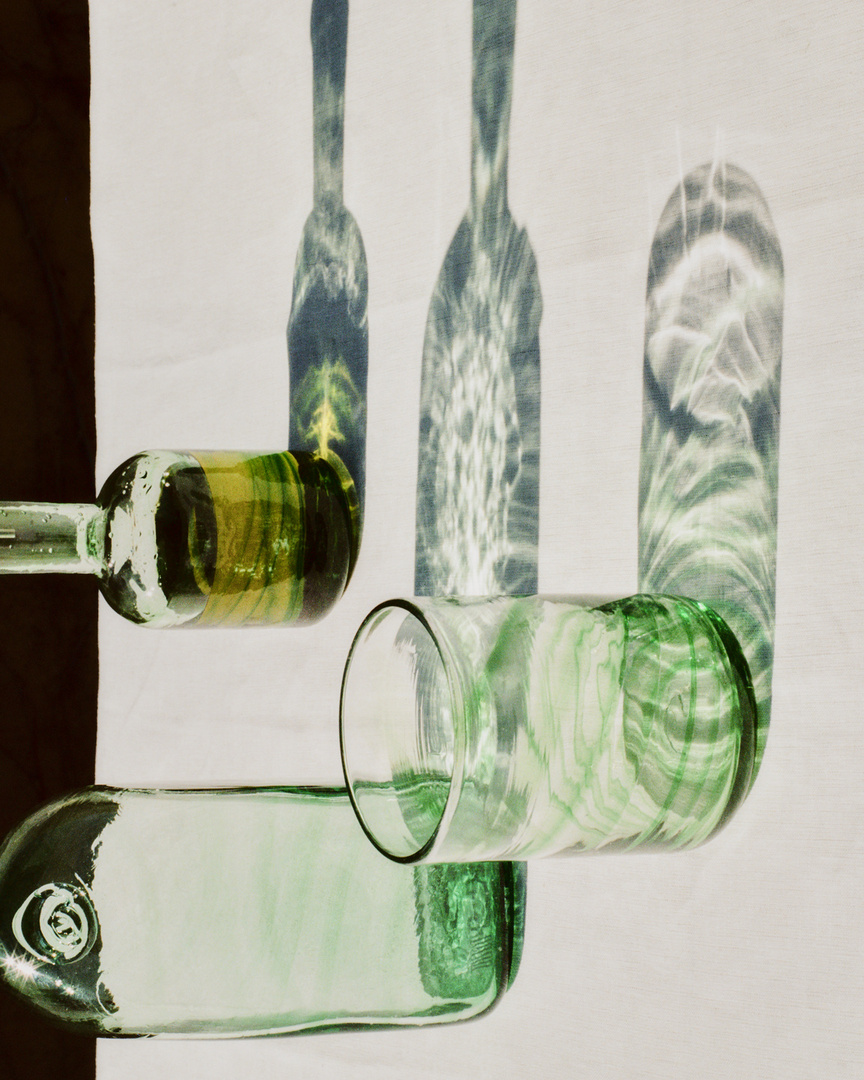 Still life shot of green and clear glass bottles in a horizontal position casting shadows on a white background, creating a visually appealing composition.