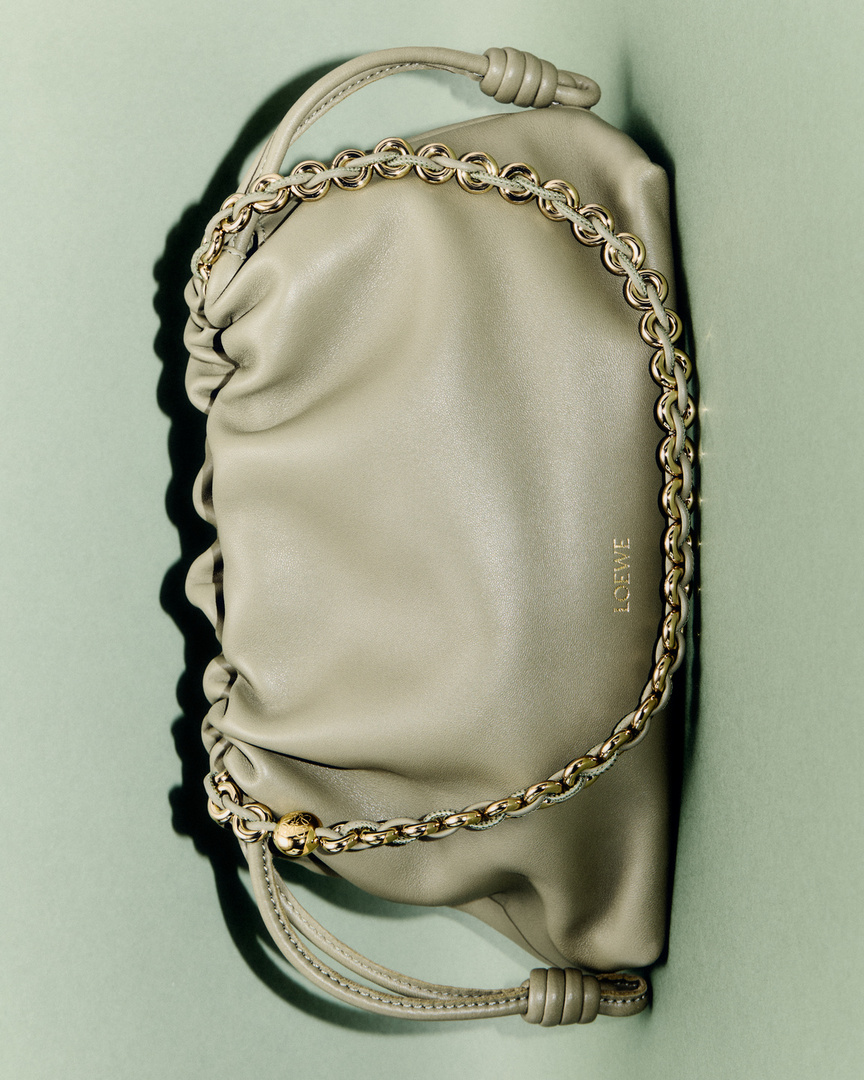 Luxurious Loewe Font Tote with gold chain strap, draped against a muted green backdrop, is the perfect accessory for any fashionable event.