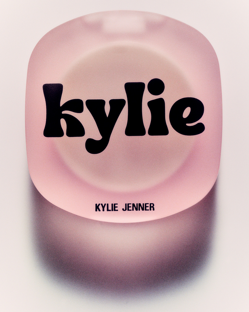 Closeup of a light pink Kylie Jenner makeup compact with black 'Kylie' font, photographed on a bright white surface.