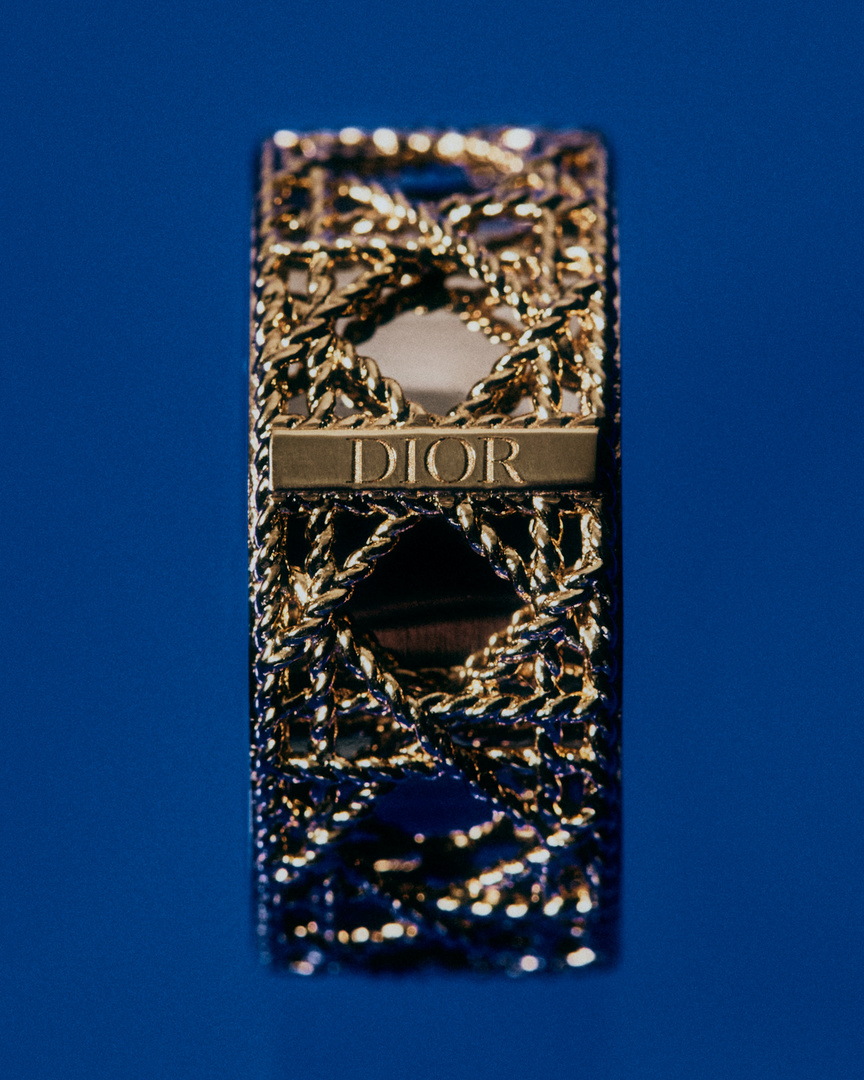 Close-up of Dior lipstick case with a gold chain pattern and the Dior logo on a blue background. Beauty and cosmetics.