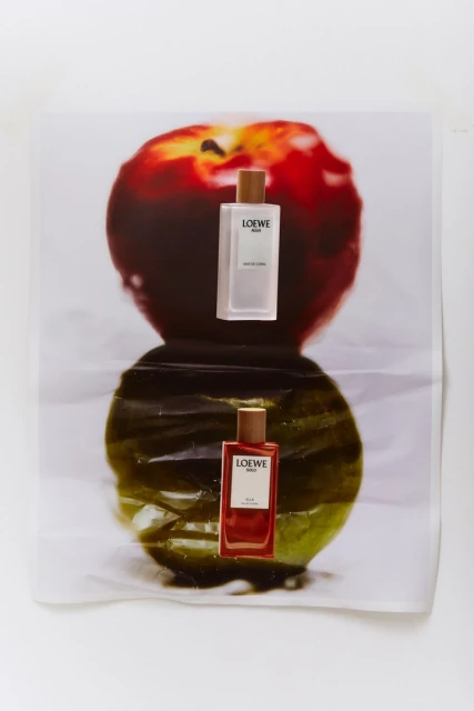 Two Loewe Solo fragrances are arranged over a printed apple image, one bottle reflecting in a glossy surface, studio lighting.