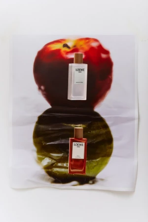 Two Loewe Solo fragrances are arranged over a printed apple image, one bottle reflecting in a glossy surface, studio lighting.