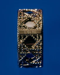 Close-up macro shot of a gold ring with intricate woven design and engraved Dior logo on a vibrant blue background.