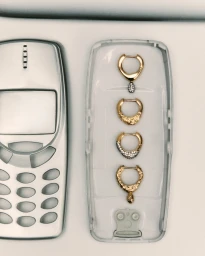 Overhead studio still life of gold earrings arranged inside a dismantled silver mobile phone case.