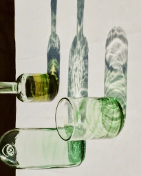 Green glass bottles and a tumbler casting shimmering water caustic shadows on a white surface