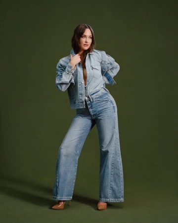 Woman in denim jacket and wide leg jeans posing against a dark olive green backdrop by Daria Kobayashi Ritch.