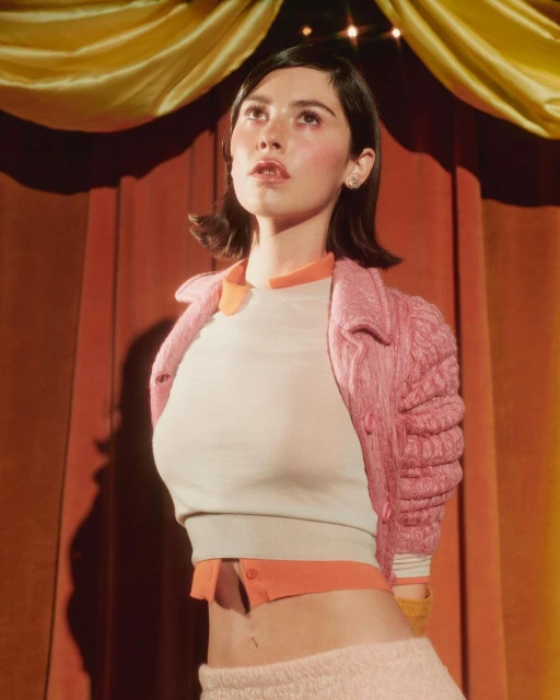Attractive woman in fashionable vintage-inspired outfit stands against curtain, looking up in a studio shot. Fashion, portrait, styling.