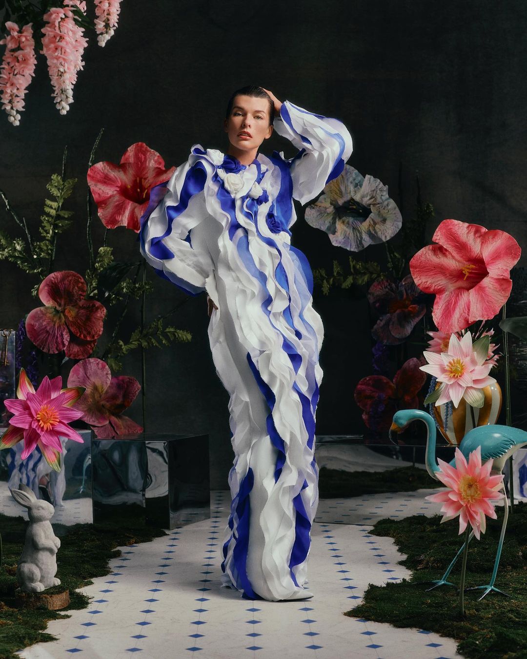 Woman in ruffle dress poses in a surreal floral garden setting.  Indoor fashion photography with a model wearing an elaborate blue and white gown.