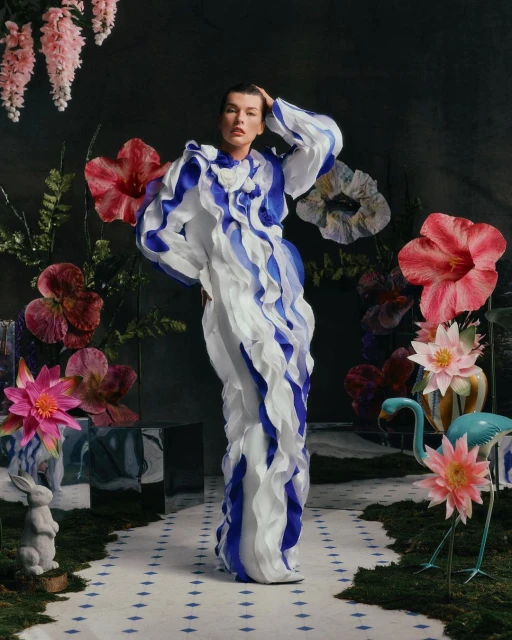 Woman in ruffle dress poses in a surreal floral garden setting.  Indoor fashion photography with a model wearing an elaborate blue and white gown.