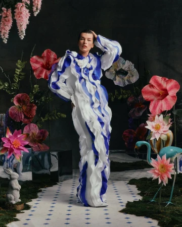 Woman in ruffle dress poses in a surreal floral garden setting.  Indoor fashion photography with a model wearing an elaborate blue and white gown.