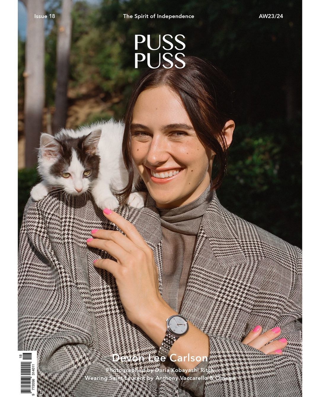 Magazine cover featuring a smiling woman with a cat perched on her shoulder, wearing a plaid jacket, with an outdoor background.