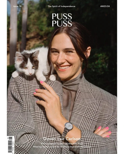 Magazine cover featuring a smiling woman with a cat perched on her shoulder, wearing a plaid jacket, with an outdoor background.