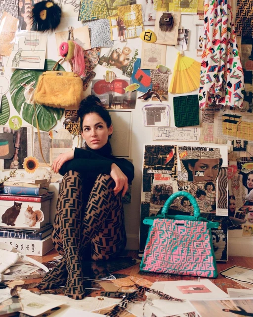 Brunette woman in Fendi print leggings and turtleneck, sitting on the floor amid colorful collages and a pink handbag. Fashionable and unique.