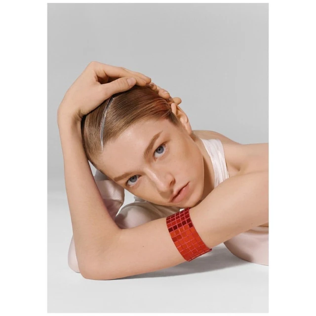 Adult female with light skin posing in a photo studio. The model is wearing a sparkling, ruby red arm bracelet and a white tank top.