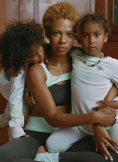 Woman and two children in activewear. An adult with two children, one child resting head on shoulder. All wear active clothing indoors.