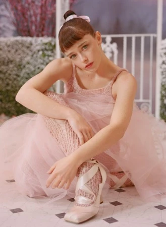 Young ballet dancer in a pink tutu and ballet slippers poses in a photo studio with a snowy outdoor backdrop, creating a surreal winter scene.