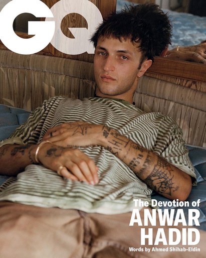 GQ magazine cover featuring Anwar Hadid reclining on a striped cushion. He wears a striped shirt and tan pants, with visible arm tattoos.