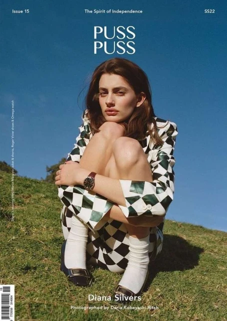 Magazine cover featuring Diana Silvers wearing a black and white checkered suit, sitting on a grassy hill against a blue sky backdrop.