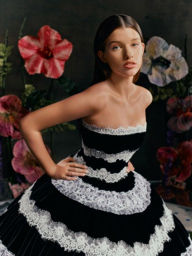 Young woman wearing a black and white strapless lace-trimmed dress posing before large decorative floral props.