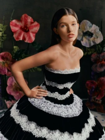 Young woman wearing a black and white strapless lace-trimmed dress posing before large decorative floral props.