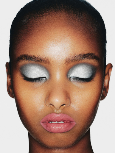 Close-up portrait of a woman with metallic silver eyeshadow and pink lips against a plain white background