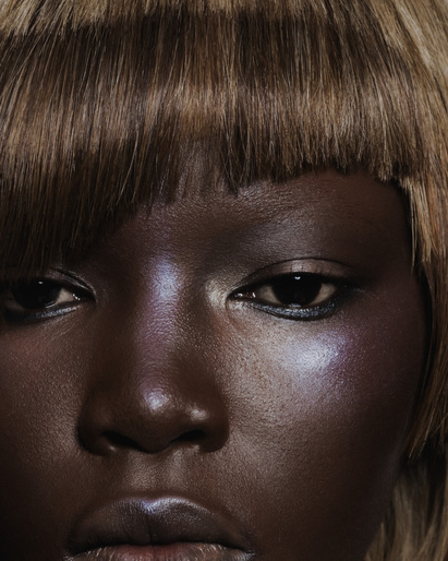 Close-up beauty shot of an African-American woman with an auburn blunt bob, highlighted cheekbones, and glossy lips in a studio setting.