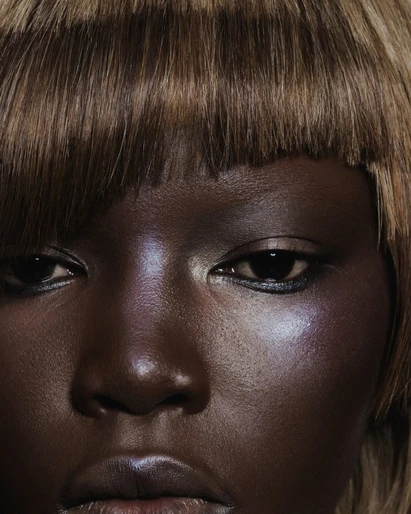 Close-up beauty shot of an African-American woman with an auburn blunt bob, highlighted cheekbones, and glossy lips in a studio setting.